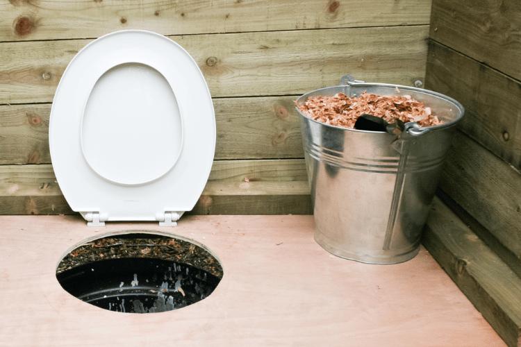 Wooden Compost Toilet with a metal bucket full of dry leaves and peat moss